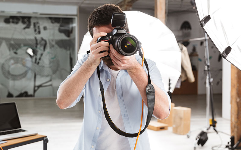 Man in a light blue color of shirt taking a picture with his digital camera | Careers Collectiv
