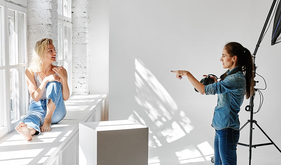 Girl photographer instructing her model for a pose in a white room | Careers Collectiv
