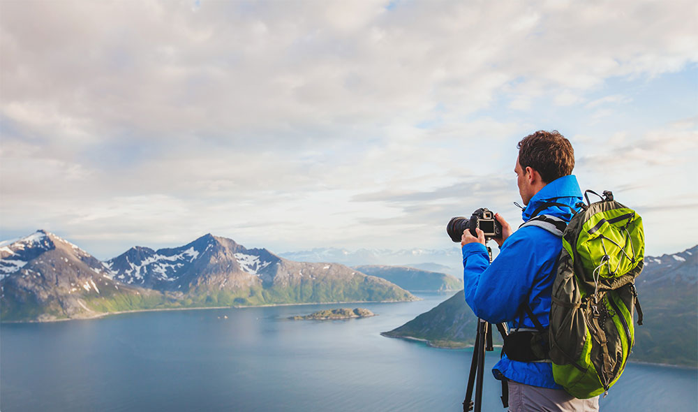 A man photographer with a blue jacket with his bag capturing a mountain hilltop | Careers Collectiv