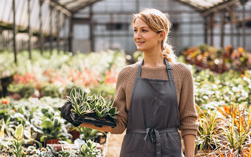 A woman in her gray apron while carrying her plant at the garden | Careers Collectiv