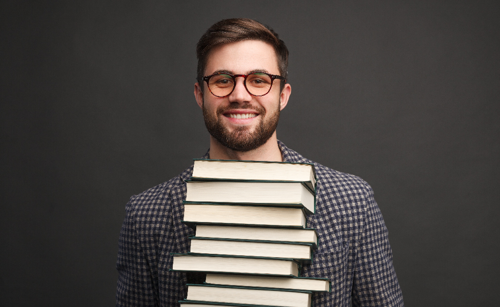 What Are The Education Requirements for CPA and Bookkeepers? - A man in an eyeglass carrying a pile of books | Careers Collectiv